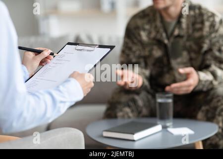 Female doctor taking notes while having conversation with veteran Stock Photo