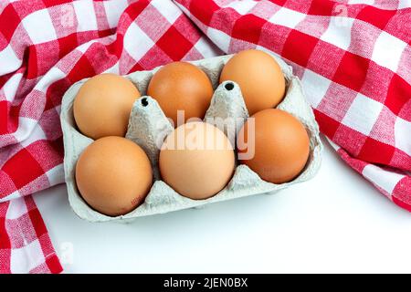 A pack of six brown organic free-range chicken eggs with a traditional red kitchen checkered towel or tablecloth on white. Stock Photo
