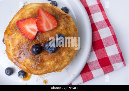 American pancakes with maple syrup, strawberries and blueberries for breakfast on a plate top view with a traditional picnic tablecloth Stock Photo