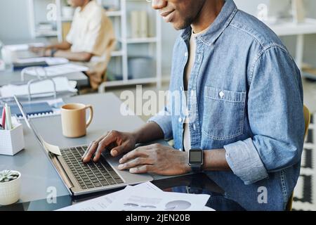 Cropped shot of young man typing at laptop keyboard in coworking space with people in background Stock Photo