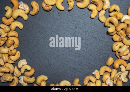 Round frame of cashew nuts top view on black slate board. Stock Photo