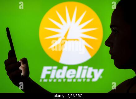 In this photo illustration, the Fidelity Investments logo is seen in the background of a silhouetted woman holding a mobile phone. Stock Photo