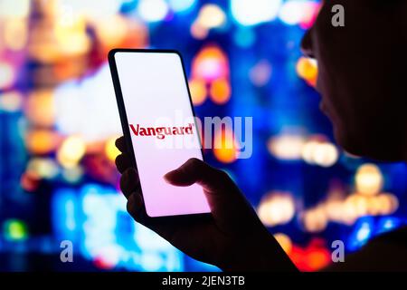 In this photo illustration, a silhouetted woman holds a smartphone with the Vanguard Group logo displayed on the screen. Stock Photo