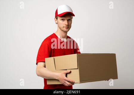 Courier man in a red uniform holding a cardboard box. Parcels Delivery Service Concept. Stock Photo