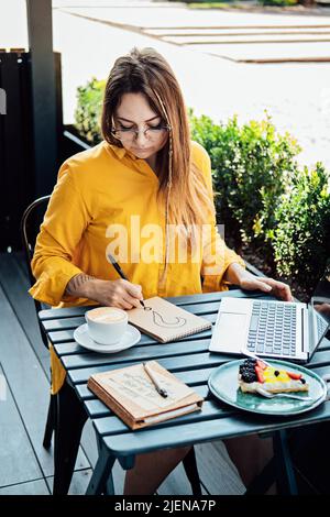 Freelancer problem challenges, Finding work, Finding clients. Freelancer woman working with laptop and writing question mark in notepad while sitting Stock Photo