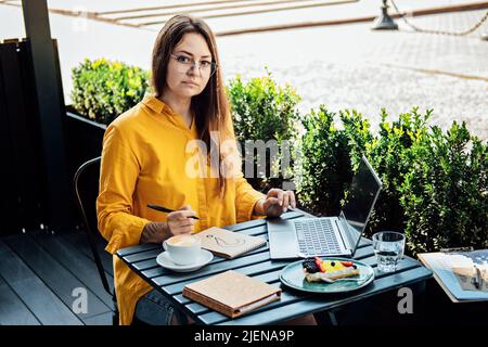 Freelancer problem challenges, Finding work, Finding clients. Freelancer woman working with laptop and writing question mark in notepad while sitting Stock Photo