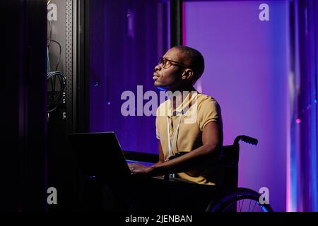 Side view portrait of male system admin with disability using computer while setting up server network Stock Photo
