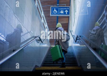 Young woman traveler tourist going up the stairs with luggage in train station. Rear view. Stock Photo