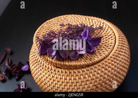 wicker straw box craft round top with dried flowers and lavender on a black background Stock Photo