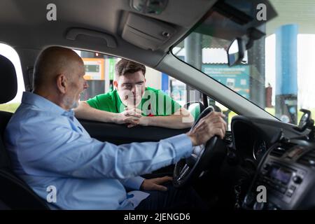 Happy employee man with Down syndrome talking with customer in car at gas station. Social inclusion concept. Stock Photo