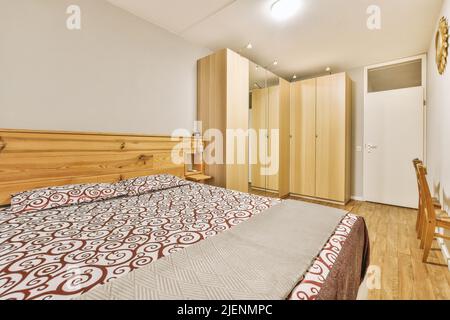 Comfortable bed with ornamental blanket placed and wardrobe with mirror in light bedroom Stock Photo