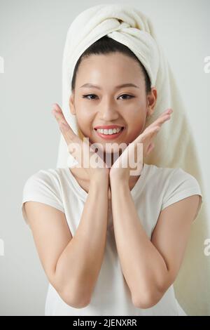 Cheerful young woman with towel on head touching her fresh glowy skin Stock Photo