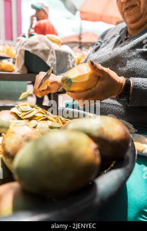 Vertical photo Closeup to the hands of a woman peeling mangoes to sell in a park in Nicaragua Stock Photo