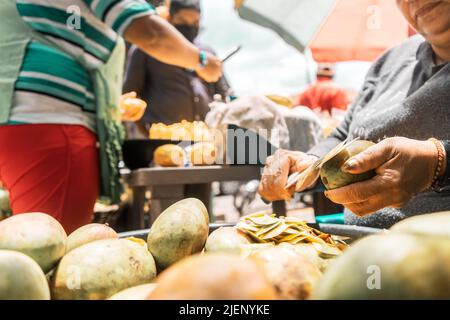 Closeup to the hands of a woman peeling mangoes to sell in a park in Nicaragua Stock Photo