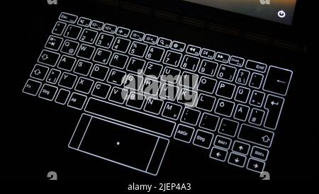Detail of a notebook with glowing keys in the dark. The power-off symbol on a screen is shown in right top of the photo Stock Photo