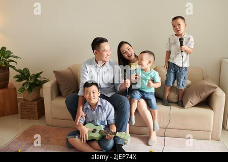 Happy family of five playing ukulele and singing song into microphones together Stock Photo