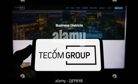 Person holding smartphone with logo of Emirati real estate company Tecom Group LLC on screen in front of website. Focus on phone display. Stock Photo
