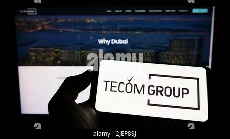 Person holding cellphone with logo of Emirati real estate company Tecom Group LLC on screen in front of business webpage. Focus on phone display. Stock Photo