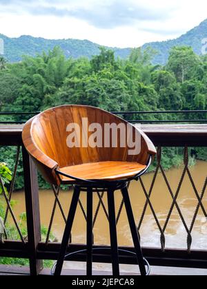 Empty round wooden bar stool made by small wood planks and black steel frame near the outdoor table bar on the terrace on green jungle, mountains and Stock Photo