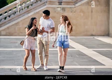 Three friends talking and laughing while walking outdoors together. Friendship and urban lifestyle concept. Stock Photo