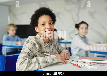 Portrait of smiling African American girl sitting at desk in school and looking at camera Stock Photo