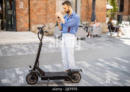 Stylish guy use phone while standing near his electric scooter outdoors Stock Photo