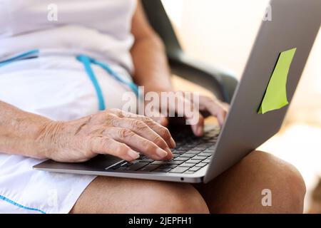 Elderly woman typing on laptop is looking for information on Internet Stock Photo