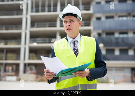 Architect in protective helmet and jacket with folder of documents on construction site Stock Photo