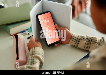 Closeup of unrecognizable child using smartphone in school classroom and hiding during class Stock Photo