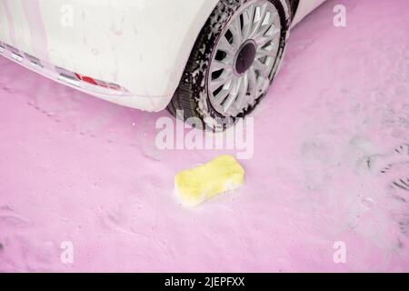 Yellow sponge in pink foam at car wash Stock Photo
