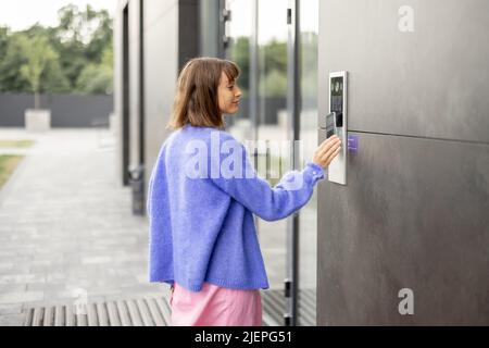 Young stylish woman getting access to the building by attaching smartphone to intercom Stock Photo