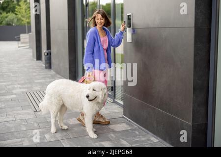 Young stylish woman getting access to the building by attaching smartphone to intercom Stock Photo