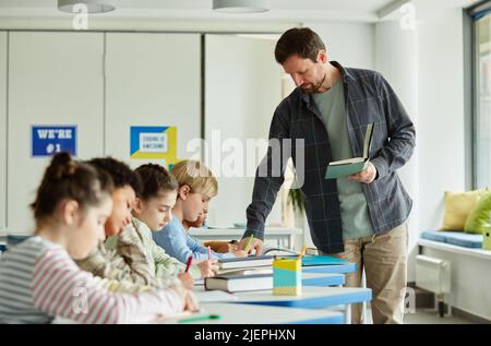 Side view portrait of male teacher helping children using computers in ...