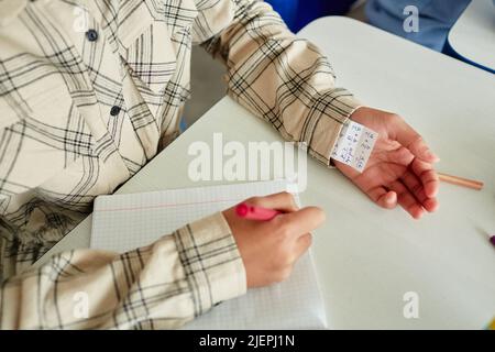 Close up of unrecognizable young child cheating during test and hiding note in sleeve, copy space Stock Photo