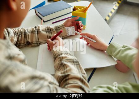 Close up of two children cheating during math test and hiding note in sleeve, copy space Stock Photo