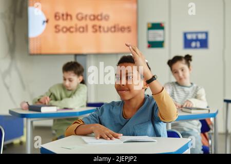 Portrait of smiling African American boy raising hand in classroom and answering question Stock Photo