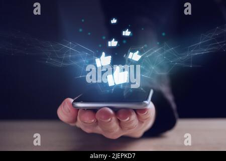 The concept of likes and successful rating on the Internet. Person with smartphone and holographic icons. Stock Photo