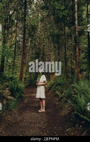 Beautiful young woman with fern leaf in hands on path through green forest Stock Photo