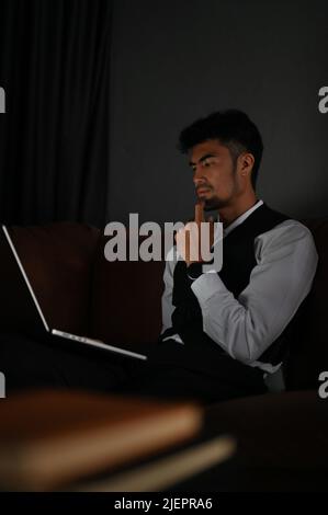 Serious and thoughtful Asian businessman or male executive manager looking at laptop screen, planning a business strategy or business problem solution Stock Photo