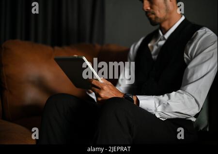 A professional Asian male executive manager or businessman sits at the leather sofa and uses a portable digital tablet. cropped image Stock Photo