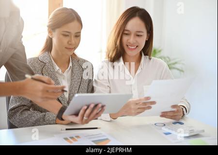 Two beautiful young Asian businesswomen in the meeting, discussing and analysing a financial and an accounts sales profit in the office. Stock Photo