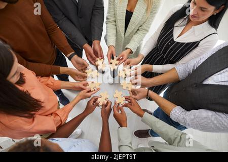 Business people or office workers hold pieces of wooden puzzles that symbolize teamwork. Stock Photo