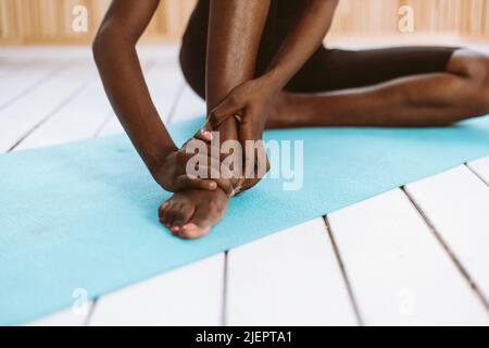 Unrecognizable barefoot dark skin multiracial woman touching feet. Stretch and do yoga. Stiff foot tendons, ligaments  Stock Photo