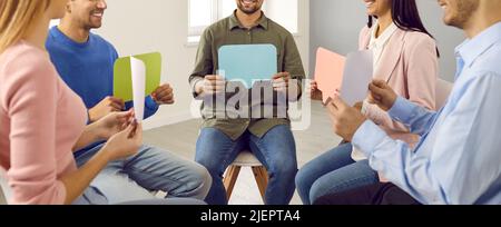 Smiling young people sitting in circle and showing each other their empty colored speech bubbles. Stock Photo