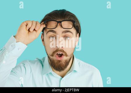 Young man lifts his glasses and looks at something with funny astonished face expression Stock Photo