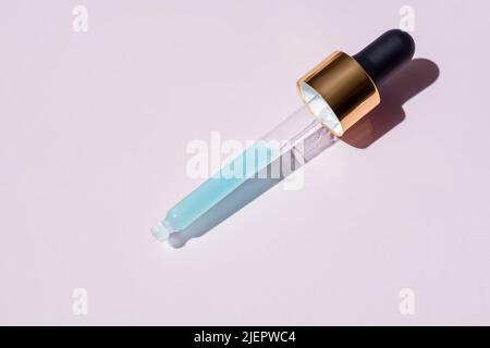 Golden pipette dropper with blue serum made of natural marine collagen on pink background Stock Photo