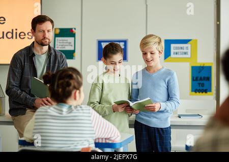 Portrait of two kids answering questions in school in front of classroom, copy space Stock Photo
