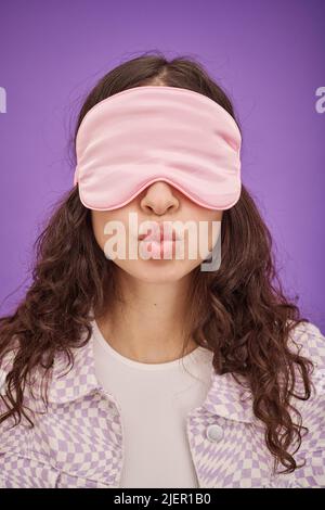 Portrait of young woman in sleep mask on her eyes sending a kiss isolated on purple background Stock Photo