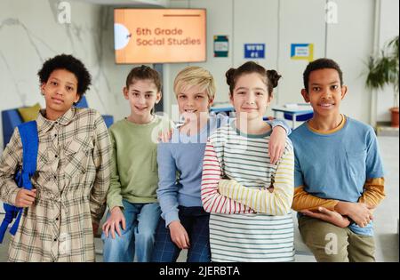 Portrait of diverse group of children looking at camera and smiling while standing together in school classroom Stock Photo