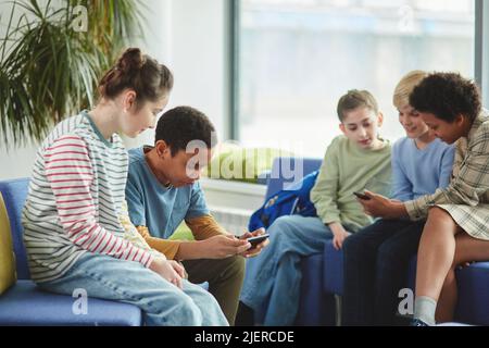 Diverse group of children using smartphones in school during break all dressed in colorful clothes Stock Photo